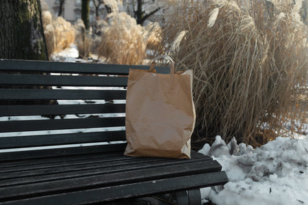 A paper bag with food products stands on a wooden bench in a winter sunny day. High quality photo