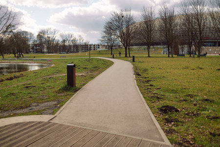 A serene view of a walking path in a park, surrounded by grass, trees, and open space. The peaceful scene highlights nature and outdoor leisure activities, ideal for walking and relaxationの写真素材