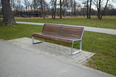 A peaceful park scene featuring a wooden bench along a walking path. The bench provides a place to relax while enjoying the view of the surrounding trees and greenery in a public parkの写真素材