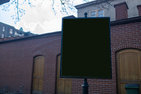 Blank signpost on a street corner stands next to a brick wall with wooden doors. The empty signboard can be used for various purposes, like inserting custom messages or advertisementsの写真素材