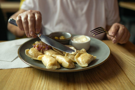 Person is holding a knife and fork, ready to eat a plate of traditional dumplings served with a side...