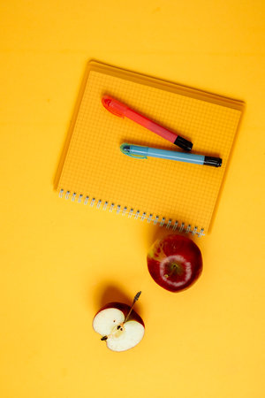 A vibrant and colorful setup featuring office supplies such as pens, sticky notes, and a notepad, complemented by a fresh red apple. The bright yellow background adds an energetic touch to the sceneの写真素材