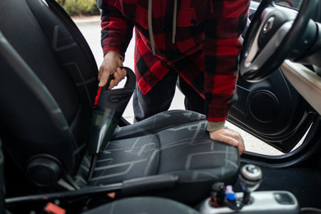 Details of car vacuum cleaning. Professional cropped male worker using wet vacuum cleaner for dirty car interior. Auto car service cleaning the drivers seat, cleaning and vacuuming concept. High quality photoの写真素材