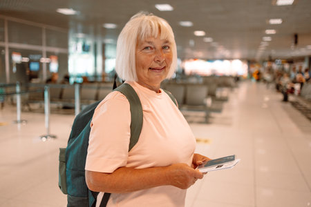 Happy blonde hair Elderly female tourist with a backpack with a passport while waiting for the passport check of the tourist at the airport. High quality photoの写真素材