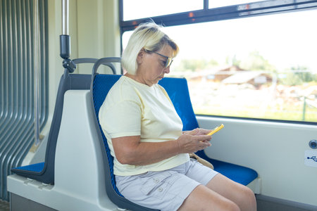 Old European woman sitting in streetcar and using smartphone while waiting for next stop and going home. High quality photoの写真素材