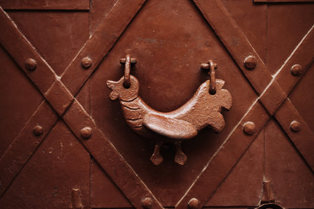 Close-up of an old-fashioned rooster-shaped door knocker on a brown iron door in Warsaw, Poland....