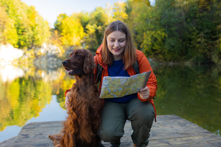Happy 30s woman hiker hiking in mountain lake. Female with a irish setter dog looking at map and planning trip or get lost. Poland. High quality photoの写真素材