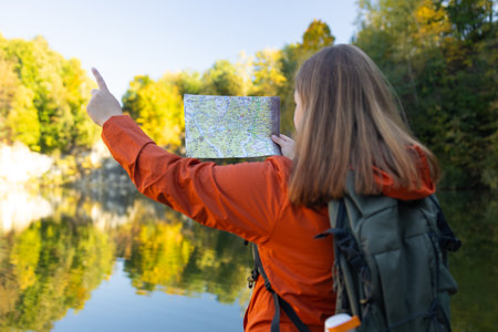 Young woman holding map searching right direction looking away in forest. Relaxed woman hiker looking navigation searching route and exploring nature.. Hiking concept. High quality photoの写真素材