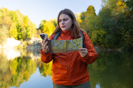 Wanderings. Stylish young woman traveler with a backpack and phone, holds a map, explores hiking trails in the mountains. The concept of travel, vacation.の写真素材