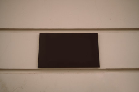 Plain black rectangular sign mounted on a beige wall. The sign is completely blank, suggesting it is either new, unmarked, or awaiting custom lettering. The minimalistic look gives it a modern and neutral appearance.の写真素材