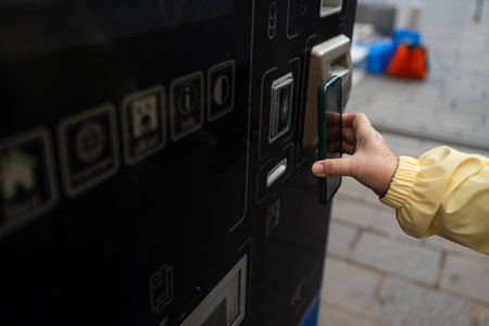 Close-up of a woman using a contactless card or phone to pay at a ticket machine in Krakow. The street scene reflects modern urban transit in Poland.の写真素材