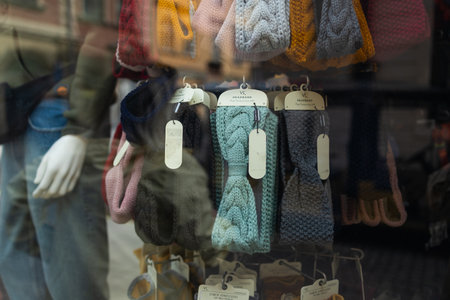 A shop window in Krakow displays colorful winter accessories, including hats and scarves. Reflections of historic buildings and a mannequin in a jacket add depth to the cozy street scene.の写真素材
