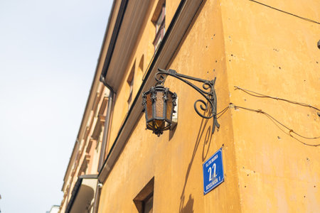An ornate street lantern is mounted on the corner of a historic yellow building in Krakow, Poland. The classic iron design and visible street number add charm to the old-town architecture.の写真素材