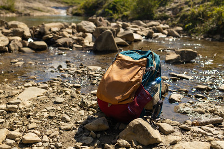 Colorful backpack resting on a rocky riverbed in a scenic mountain valley under blue skies. Symbol of adventure, hiking, solo travel, and connection with nature. Perfect for outdoor lifestyle, tourism, and exploration themes.の写真素材