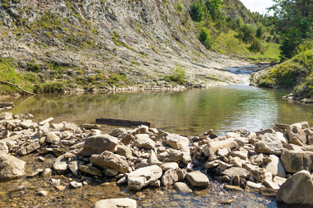 Serene mountain creek winding through a rocky valley with clear water, surrounded by greenery and steep slopes. Captures the raw beauty of untouched nature, perfect for themes of tranquility, ecology, hiking, or travel.の写真素材
