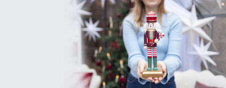Woman showing wooden nutcracker toy in front of camera. Christmas tree, lights, and stars on background create cozy holiday mood. Concept of Christmas tradition, festive decoration, celebration, and winter holidays.の写真素材