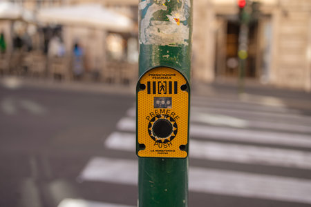 Close-up of a pedestrian crossing button on a pole near a zebra crosswalk on a city street in Rome,...