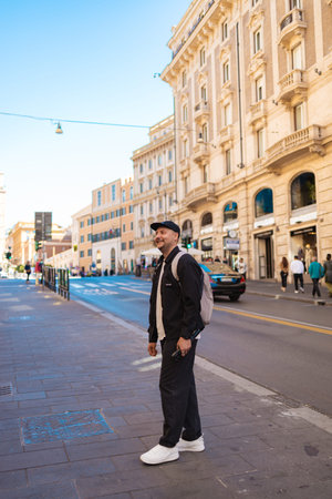 Rome, Italy - October 4, 2025: A tourist with a backpack walking along a city street in Rome, surrounded by historic architecture and urban traffic, capturing everyday travel and city life in the Italian capital.のeditorial素材