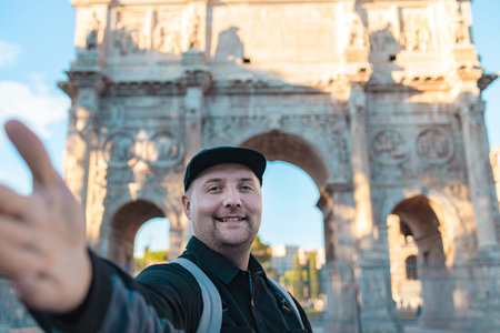 Smiling male tourist taking a selfie in Rome, Italy during sightseeing trip. Travel lifestyle, vacation in Europe, historic architecture and tourism concept. Happy traveler exploring the Italian capital on a sunny day.の写真素材