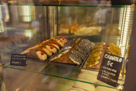 Traditional Italian cannoli pastries with various toppings displayed in a bakery glass showcase,...