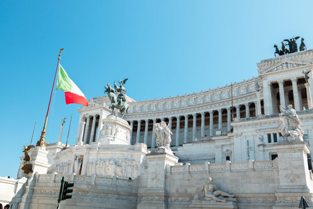 Rome Italy October 3 2025 - Monumental white marble architecture with Italian flags waving in front of the Altare della Patria Vittoriano monument under clear blue sky in central Rome.のeditorial素材