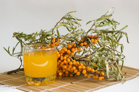 the Image of a glass with juice against sea-buckthorn berries branch