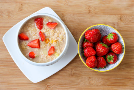 A bowl of hot oatmeal with fresh strawberries for a healthy breakfast with a bowl of strawberries.