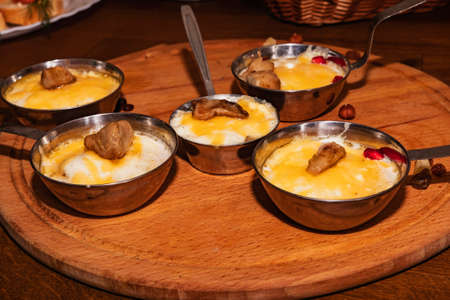 Tasty hot julienne with mushrooms and white sauce in iron cocktails on a round wooden board. A traditional dish of mushrooms, cheese, meat and sauce baked in a bowl in a rustic restaurant on the table.の写真素材