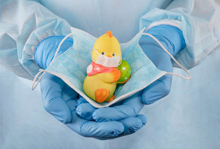 Medic's hands in protective gloves hold a teddy chicken in a medical mask. quarantined child protection. Stop coronavirus concept. Self-isolation, social distance and quarantine during a pandemicの写真素材