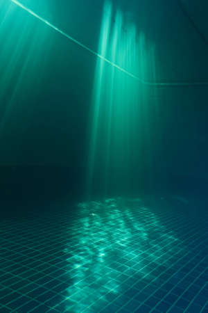 The magic rays of sunlight in the depths. Background, texture. Blurry. Underwater photo of sunlight in a deep pool. A place for jumping, diving, active sports and fitness in the water.の写真素材