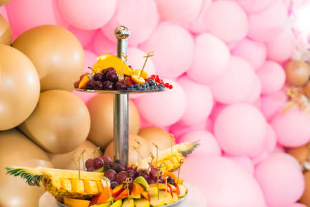 Decoration with pink and gold balloons for celebrating a birthday anniversary wedding. Soft focus. Candy bar with sweets and fruits. Treats for guests strawberries pineapple cherries blueberries.の写真素材