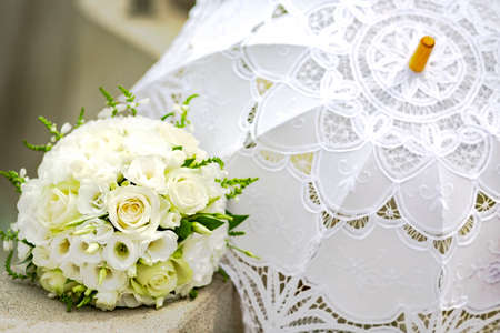 Wedding arrangement. Luxurious bride's bouquet of white roses and eustomas and a white lace umbrella. Exquisite bride wedding accessories. Floristic decorの写真素材