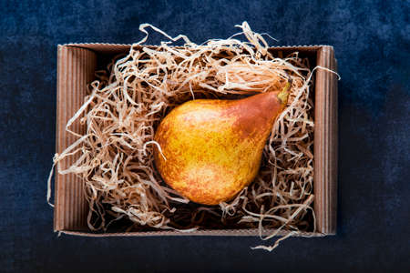 Bright, ripe, juicy orange pear Berra in a craft cardboard box in the hay. Eco-friendly packaging without plastic. Yellow pear in a box on a dark background. Place under the text. Copyspaceの写真素材