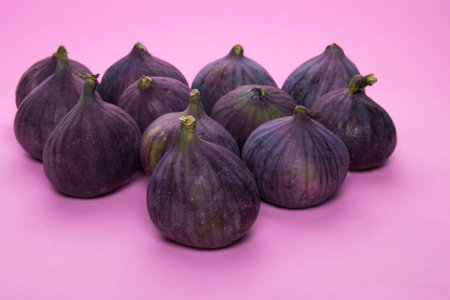 12 beautiful ripe purple figs are on a purple pink table. Several useful summer fruits on a bright...