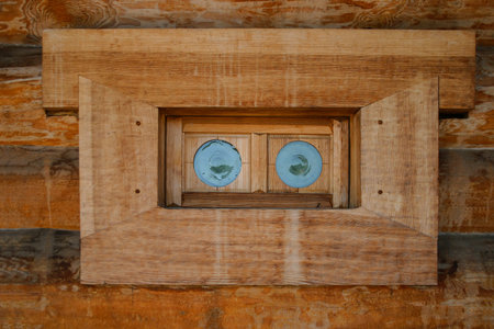 An old wooden window with small round colored glasses in a wooden house of logs. Traditional wooden...