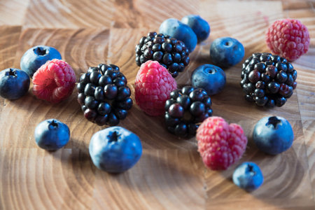 Bright ripe berries from the garden are scattered on a wooden table. Blueberries, blueberries,...
