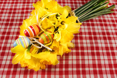 Festive Easter card. Easter bouquet of yellow daffodils and hand-painted eggs on a table with a checkered tablecloth. Place for your text. Spring bouquets of yellow flowers on the tableの写真素材