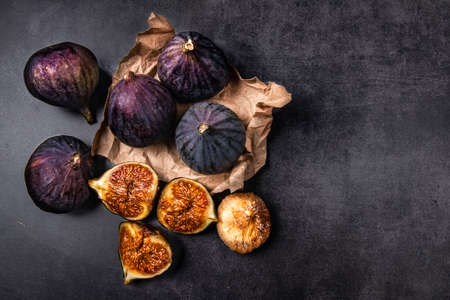 Fresh and dried figs on a dark background. Several ripe figs, one cut and dried figs lie on a dark concrete background and craft paper packaging. Still life with healthy fruitsの写真素材