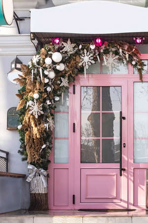 Winter festive decoration of a pink door for the New Year with branches of a Christmas tree, snowflakes, toys, bells and garlands. Christmas composition for home decoration for winter holidaysの写真素材
