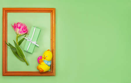 Greeting spring card for Easter, Mother's Day. beautiful spring composition. Wooden frame of a lively terry tulip, packed in green paper, a gift and a figurine of a chicken with an Easter eggの写真素材
