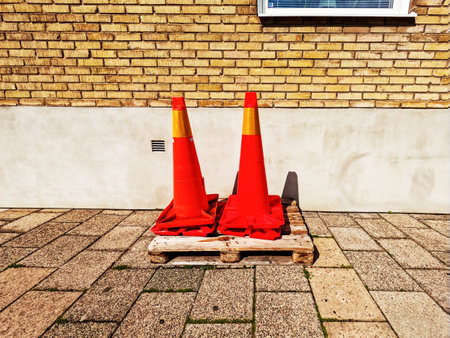 Large red traffic cones stand on a wooden pallet in front of a house. Road construction equipment. Cone for marking roads during repairs and fencing off accident sites.の写真素材
