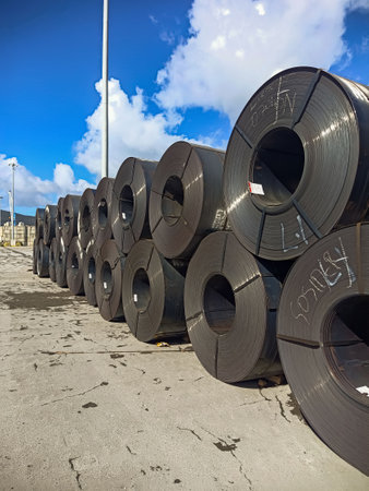 Cold rolled steel coils lie on a dock at a port before being loaded for shipment to customers. Large coils of sheet steel are stored in an open warehouse at the port.の写真素材