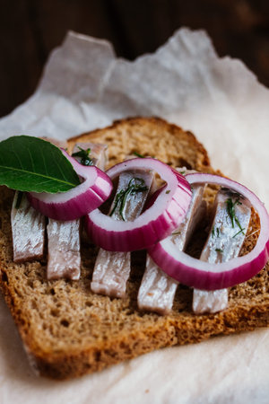Sandwich with herring, red onion, rye bread on a brown tableの写真素材