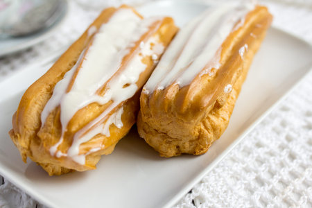 Dessert Eclair with whipped cream and sugar icing on a white table
