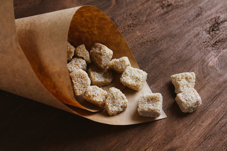 Brown unrefined cane sugar on a dark background in a paper bag. Selective focus. Toning.の写真素材