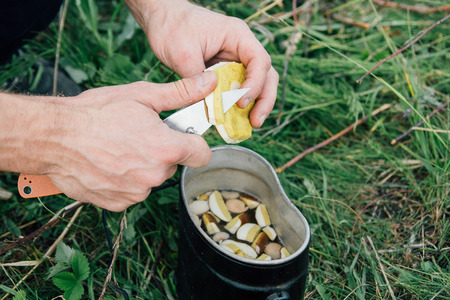 A man cuts a mushroom in nature for the soup in the potの写真素材