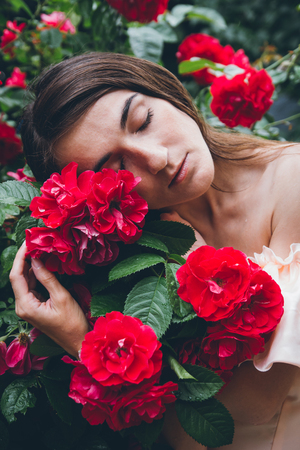 Girl with freckles stands against a background bushes with red roses. The toning. Selective focus.の写真素材