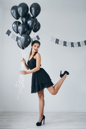 Young beautiful girl in a black dress with black balloons. Toning.の写真素材