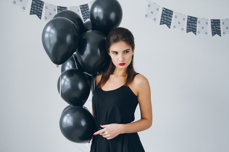 Young beautiful girl in a black dress with black balloons. Toning.の写真素材