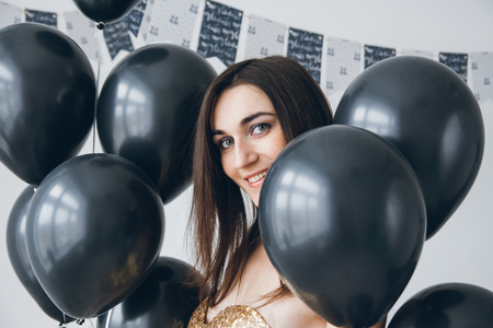 Young beautiful girl in a gold dress with black balloons. Toning.の写真素材